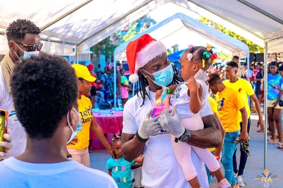 A volunteer in a Santa hat giving a gift to a child at a foundation holiday event